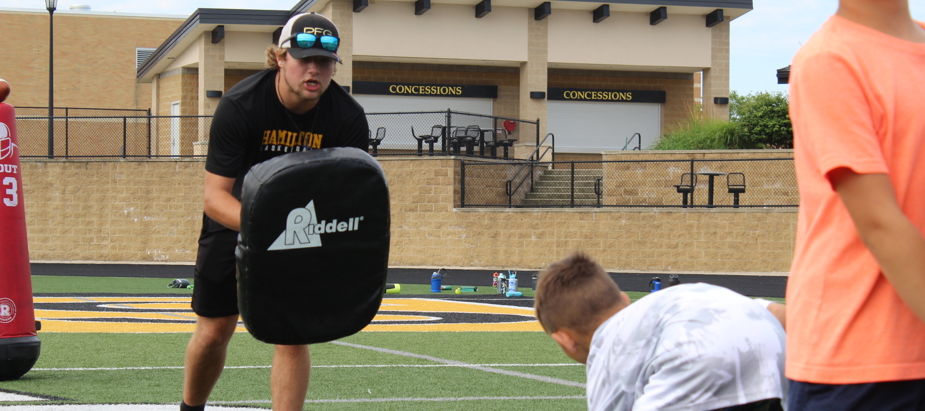 A varsity football player coaches up the players at the 'Kids Day' camp.